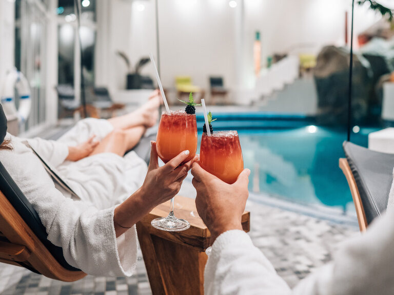 Zwei Personen stoßen mit Cocktails am Pool des Hotel Wutzschleife in Rötz an.