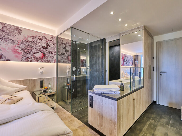 Elegantes Hotelzimmer mit Doppelbett, Spiegelwänden und offenem Badbereich.