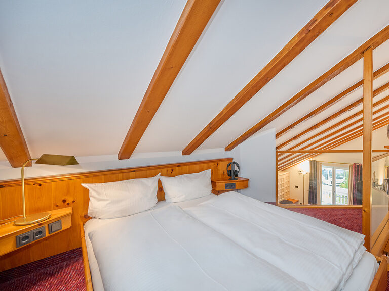Nahaufnahme eines Doppelbetts auf Empore unter Dachschräge mit Blick nach unten.
