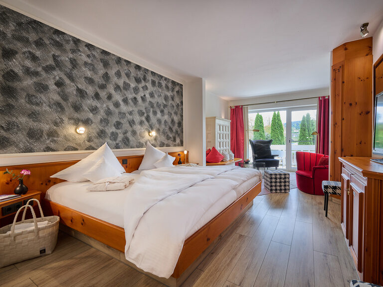 Zimmer mit Doppelbett, rustikalen Holzmöbeln, TV und Sitzbereich, Balkonblick ins Grüne.