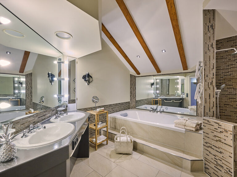 Badezimmer mit Badewanne, Dusche, Doppelwaschbecken und Dachschräge mit Balken.