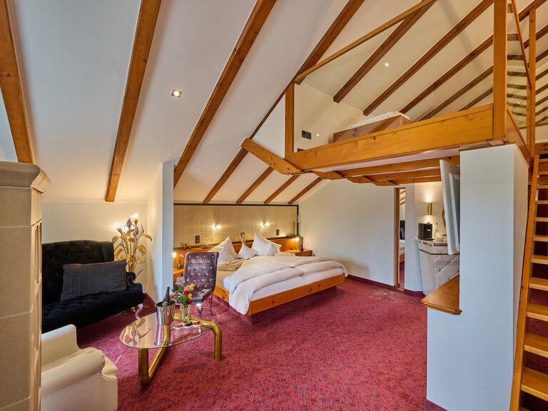 Großzügiges Zimmer mit Doppelbett, Empore, Treppe und Sitzecke unter Dachschräge.
