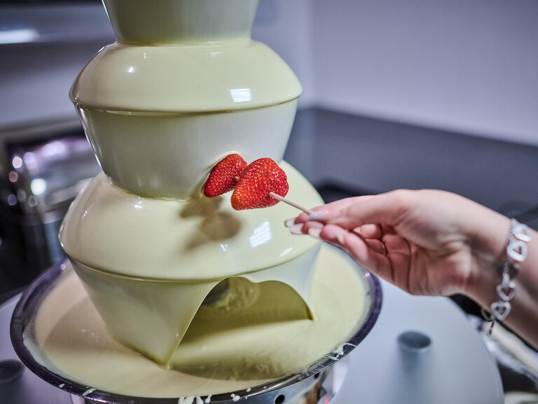 Erdbeeren am Spieß werden in weißen Schokoladenbrunnen getaucht.