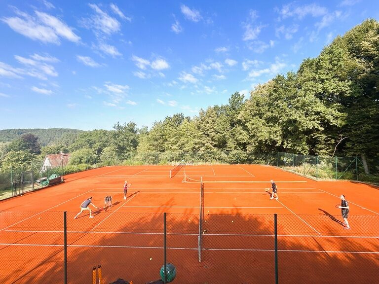 Tennisplatz im Freien mit vier Spielern auf rotem Sandbelag.