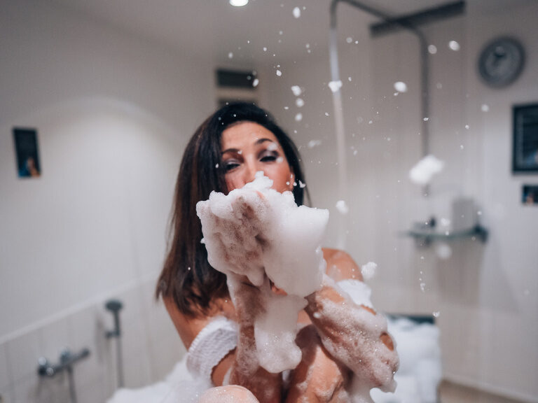 Frau in Schaumbad spielt mit Seifenblasen bei wohltuender Wellnessbehandlung.