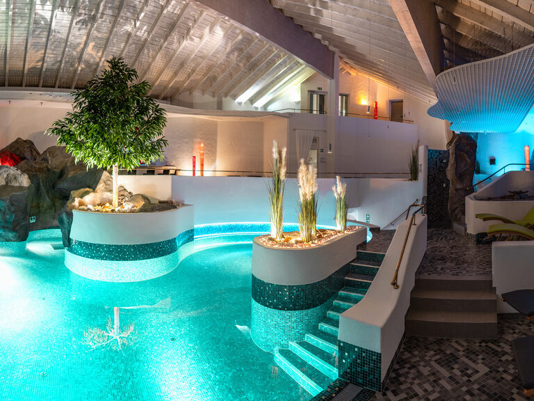 Beleuchteter Spa-Innenpool mit Pflanzeninseln, Naturstein und weißen Wänden.