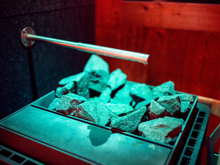 Aufgussrohr tropft Wasser auf heiße Saunasteine im stimmungsvoll beleuchteten Raum.