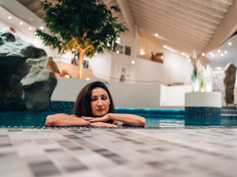 Wellnessbereich mit Frau im Wasser, Kopf auf den Armen, entspannte Atmosphäre im Innenpool.