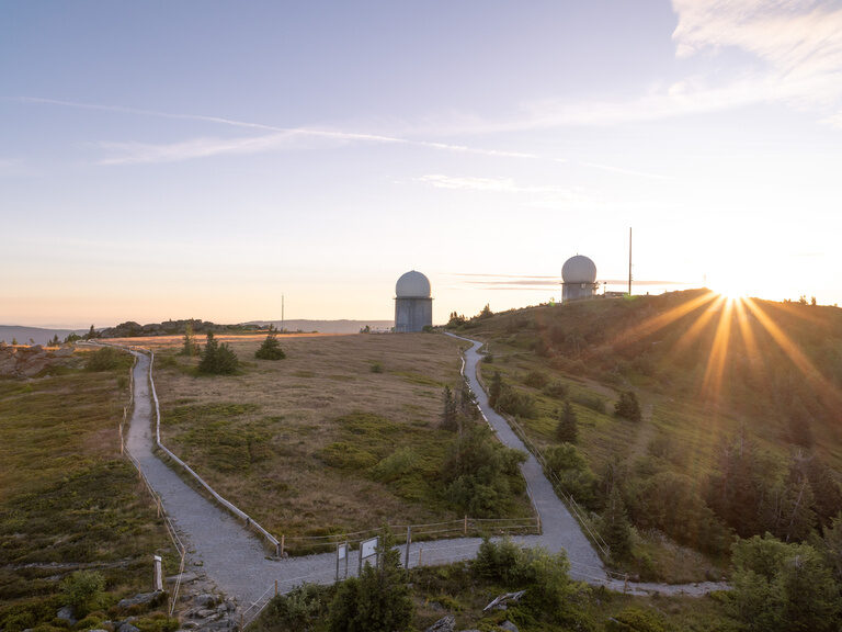 Radarstation bei Sonnenuntergang in Hügellandschaft mit Wanderwegen.