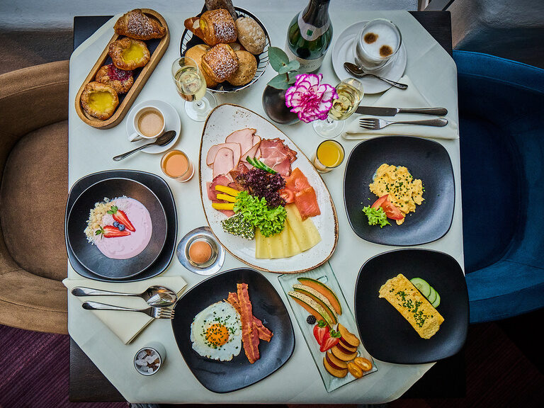 Reich gedeckter Frühstückstisch mit Aufschnitt, Eierspeisen, Joghurt und frischem Obst.