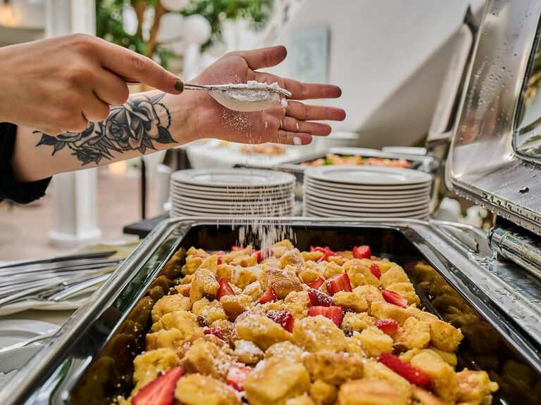 Puderzucker wird über Kaiserschmarrn mit Erdbeeren am Buffet gestreut.