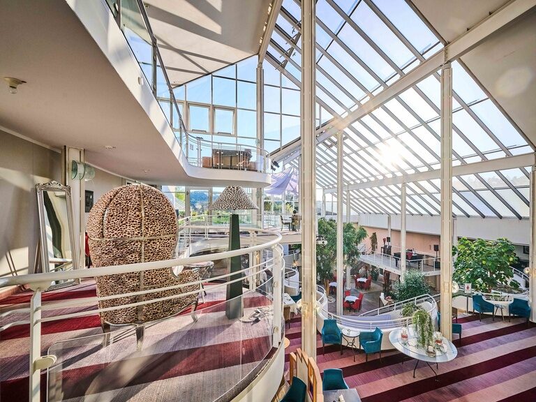 Moderne Hotel-Lobby mit Glasfassade, Hängekorb-Sesseln und viel Tageslicht.