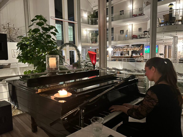 Frau spielt Klavier bei Kerzenschein in stilvoller Hotellobby.