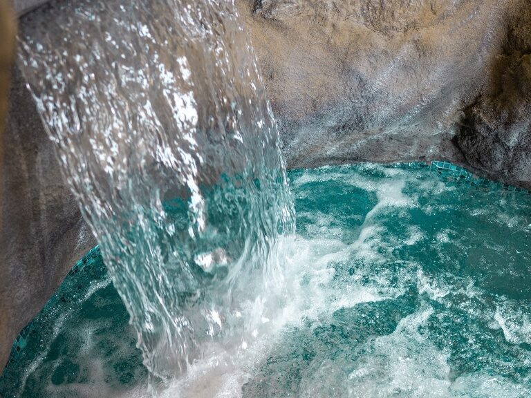 Künstlicher Wasserfall in Felsstruktur ergießt sich sprudelnd in ein kleines Becken.