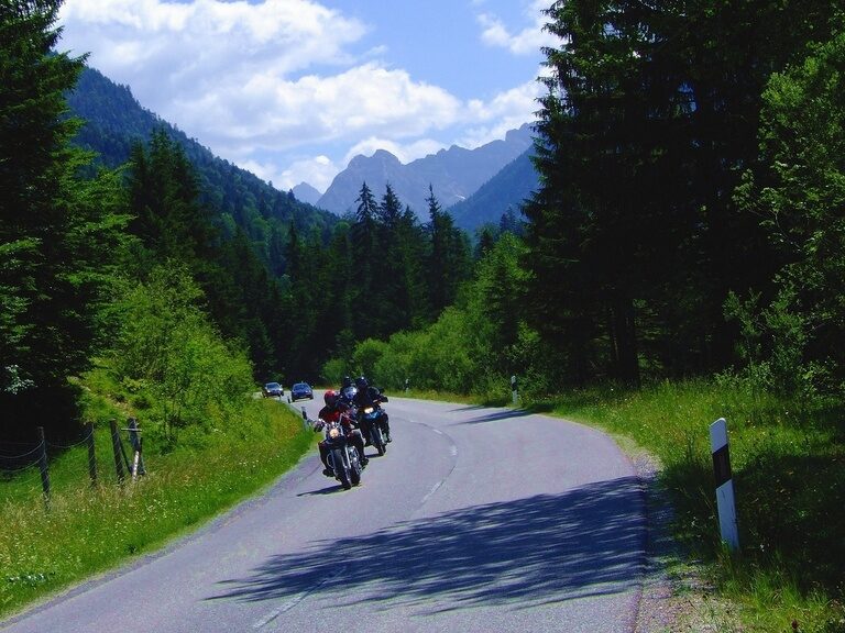 Gruppe von Motorradfahrern auf kurviger Straße im bewaldeten Alpengebiet.