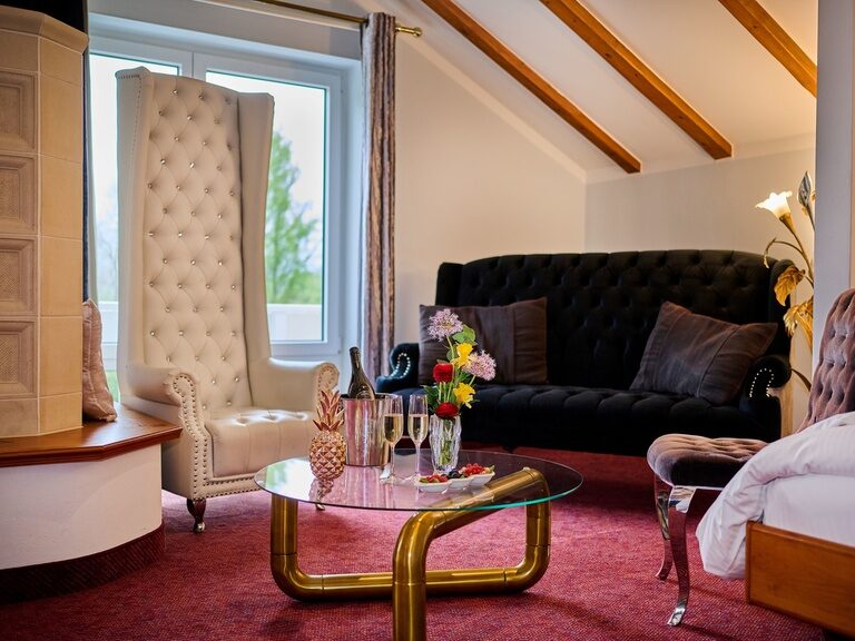 Wohnbereich mit schwarzem Sofa, weißem Sessel und Tisch mit Champagner.