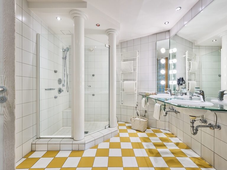 Großzügiges Badezimmer mit gelb-weißen Fliesen, Glasdusche und Spiegelwand.
