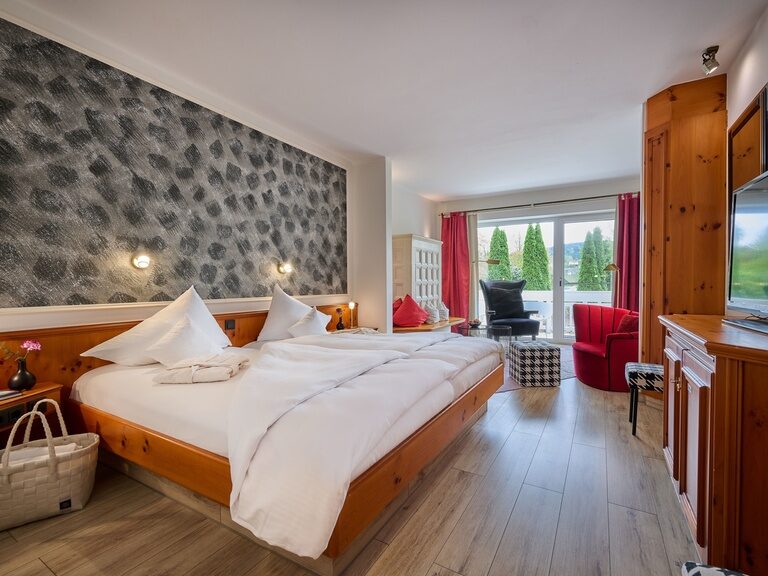 Elegantes Hotelzimmer mit Doppelbett, Holzverkleidung, Sitzbereich und Gartenausblick.