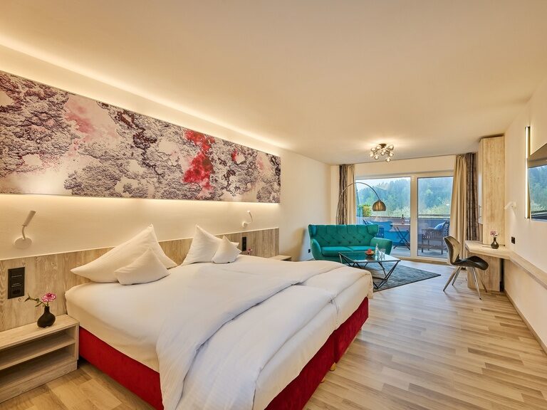 Großzügiges Hotelzimmer mit Doppelbett, Sitzecke und Balkonblick ins Grüne.