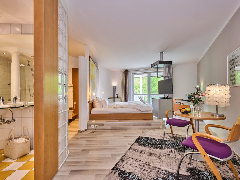 Offenes Hotelzimmer mit Sitzbereich, hellem Bad und großen Fenstern.