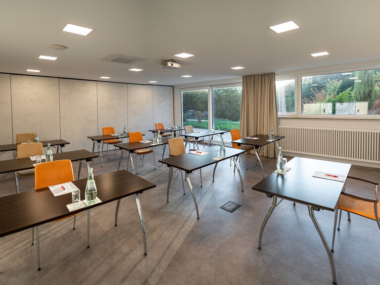 Schulungsraum mit bodentiefem Fenster, Tischen in Reihenaufstellung und Vorhängen.