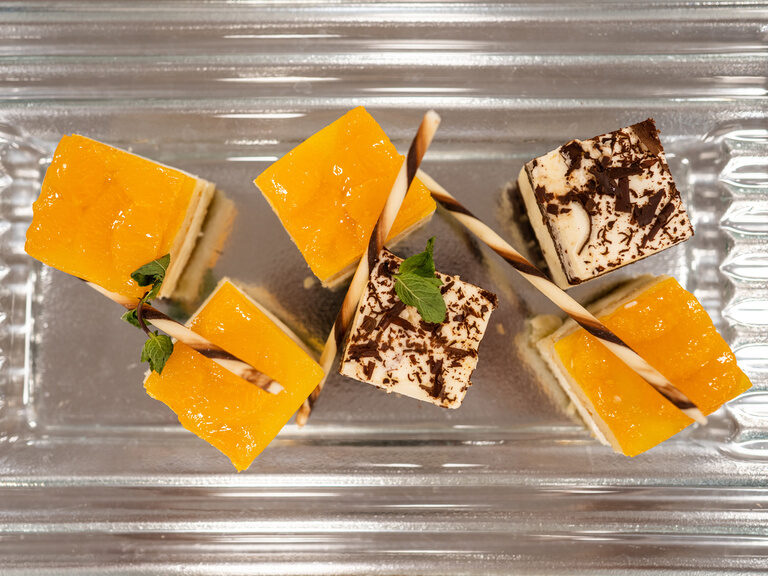 Kleine Frucht- und Schokodesserts mit Minze und Schokosticks auf Glasplatte arrangiert.