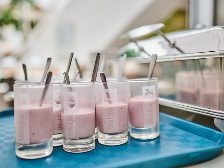 Gläser mit rosa Joghurt und Löffeln auf blauem Tablett.