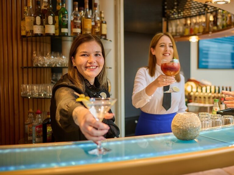 Zwei Personen stoßen mit Cocktails im am Pool des 4 Sterne Hotels im bayerischen Wald an.