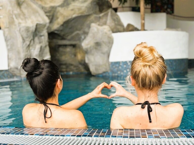 Zwei Personen stoßen mit Cocktails im am Pool des 4 Sterne Hotels im bayerischen Wald an.