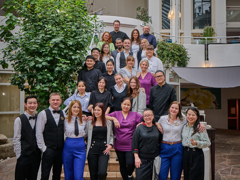 Das Team des 4 Sterne Hotels im bayerischen Wald posiert gemeinsam auf Hoteltreppe in der Lobby.